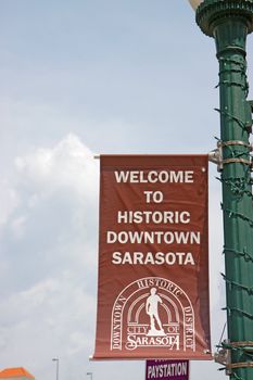 Sign saying Welcome to Historic Downtown Sarasota, Florida, in the center of the city against a blue sky and white clouds with space for text