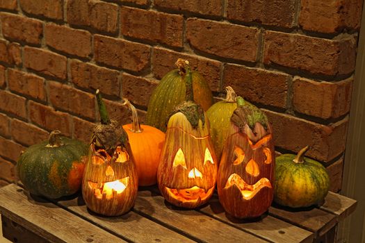 Carved eggplant jack o'lanterns with pumpkins and other squashes on a small table in front of a brick wall form part of a display for the halloween holiday