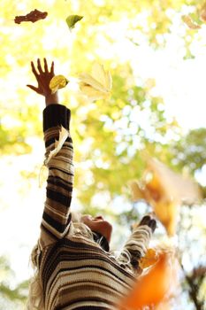 woman drop up leaves in autumn park