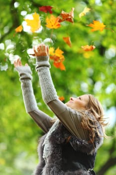 woman drop up leaves in autumn park