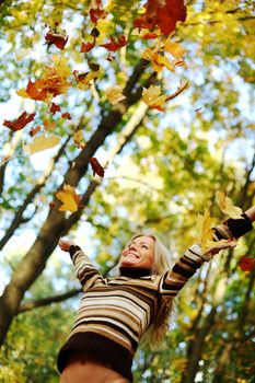 woman drop up leaves in autumn park