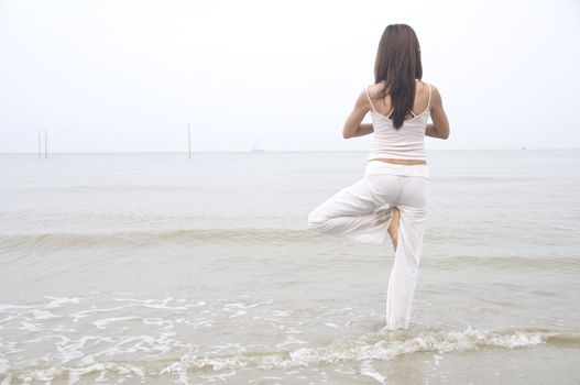 asian girl performing yoga on a beach