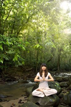 an asian female practising yoga inside a beautiful green forest