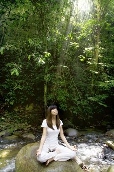 asian girl performing yoga on a rain forest with ray of lights