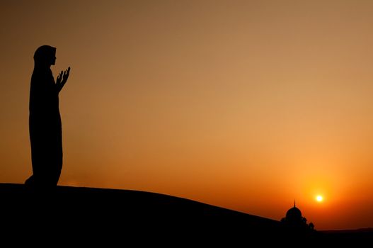 silhouette of a muslim woman praying on the desert