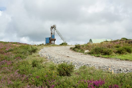 A rough track cuts through scrubland towards a blue covered minehead winding gear structure.