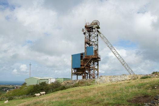 A winding gear tower structure at a minehead with wheel and support against a cloudy sky.