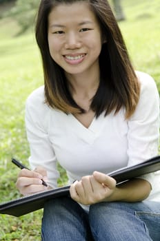 asian girl using notebook on outdoor green grass