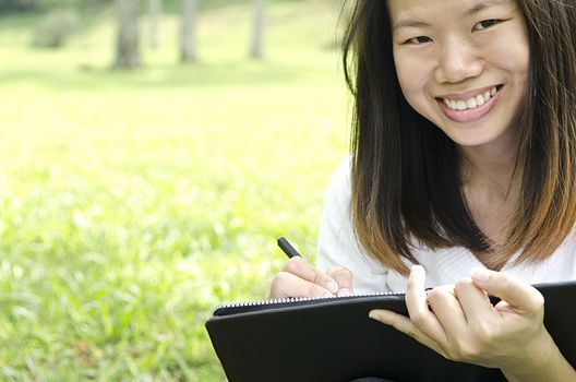 asian girl using pen and notebook whilte studying outdoor