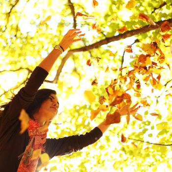 woman drop up leaves in autumn park