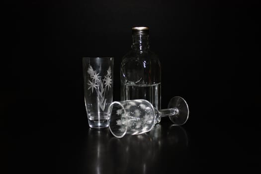Cut-glass ware and bottle with vodka over black.