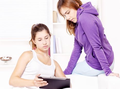 Two teenage girls using tablet computer at home