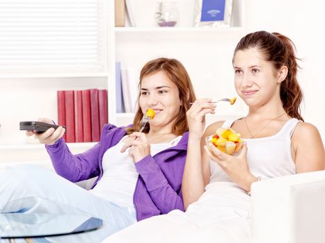 Teenage girls watching tv on the sofa and eating fruit salad