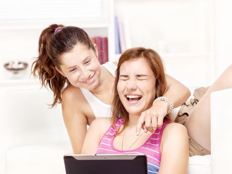 Two happy teenage girls using tablet computer at home