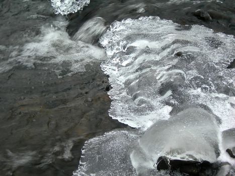 Brook is covered by icicles and water flows under them with a small strem          