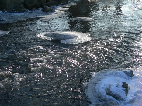 Brook is covered by icicles and water reflects sun rays          