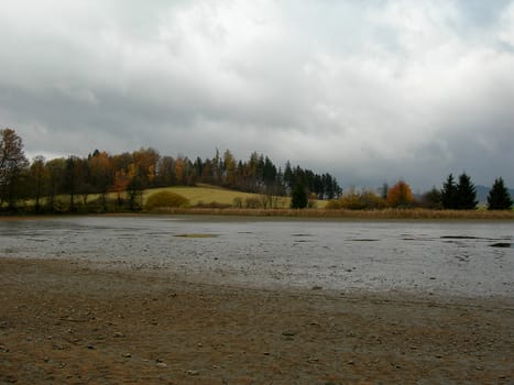           Fall landscape with forest and a pond in the foreground and dramatic sky          