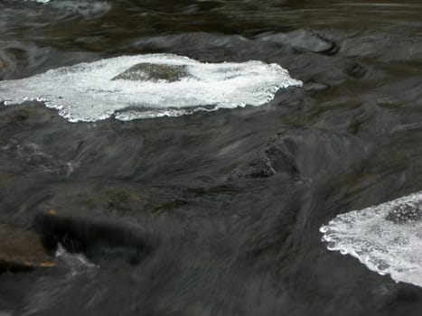 Flowing water in a brook is covered by clear ice