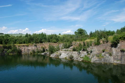 Old flooded quarry with calm water and growing trees