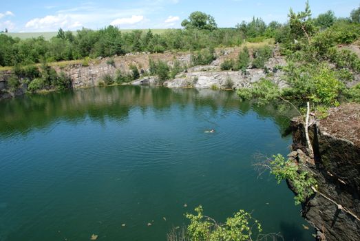 Old flooded quarry with calm water and growing trees