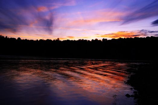                     Sun is setting behind forest and is mirroring in the lake