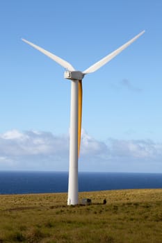 Wind generator spins in an open field overlooking Pacific Ocean