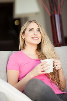 young beautiful woman with a cup on sofa at home