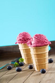 two standing waffle cones with  blueberry ice cream on wooden background