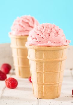 closeup of a raspberry ice cream in a waffle on white wooden background