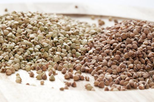 Untoasted and toasted buckwheat or kasha on a wooden plate.