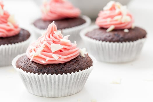 Chocolate cupcake topped with pink icing and sprinkled with white chocolate flakes.