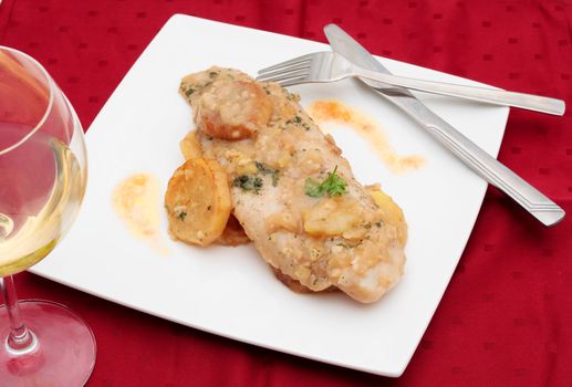 fish dish cooked in green sauce with potatoes and a glass of wine on tablecloth covered red Bordeaux