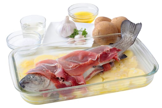 fresh trout with slices of ham on a layer potatoes and all the ingredients necessary for its preparation to the oven