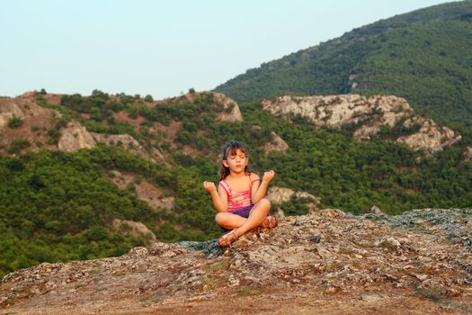 little girl sitting on a mountain top and meditate