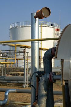 View across pipework of large steel storage tanks at a petrochemical refinery used for storing fuel and gas before distribution