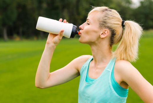 Young beautiful blond woman drinking water at summer green park