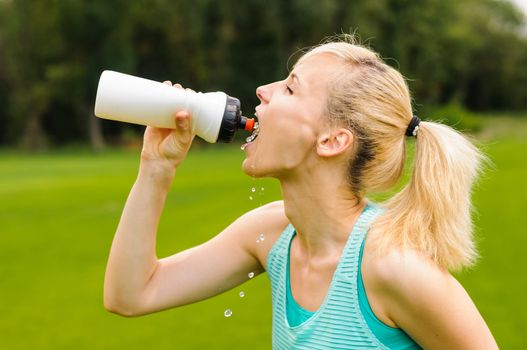 Young beautiful blond woman drinking water at summer green park