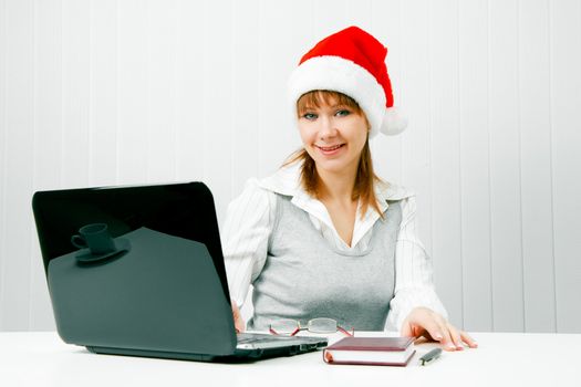 Smiling girl in a Christmas hat with a laptop at the office