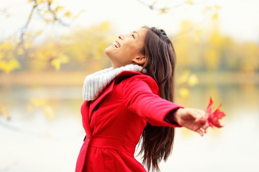 Happy autumn woman blissful and playful smiling with arms out holding red fall leave by lake.