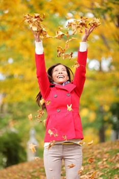 Happy fall woman throwing autumn leaves up in the air smiling blissful and cheerful in autumn forest. Young beautiful multicultural Caucasian / Asian woman model outside.