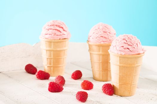 three raspberry ice cream waffle cones with raspberries on white wood