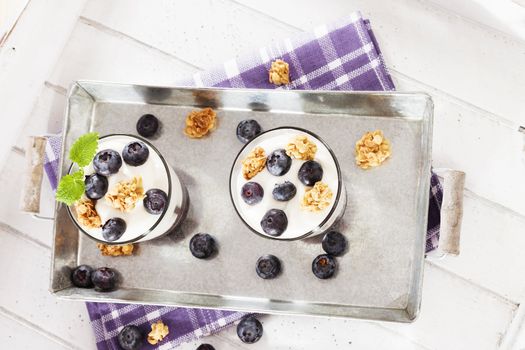 two yoghurt desserts with blueberries aside from top on a metal tray with white wood