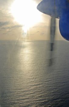 The plane is flying towards the sun over the ocean - prop is visible