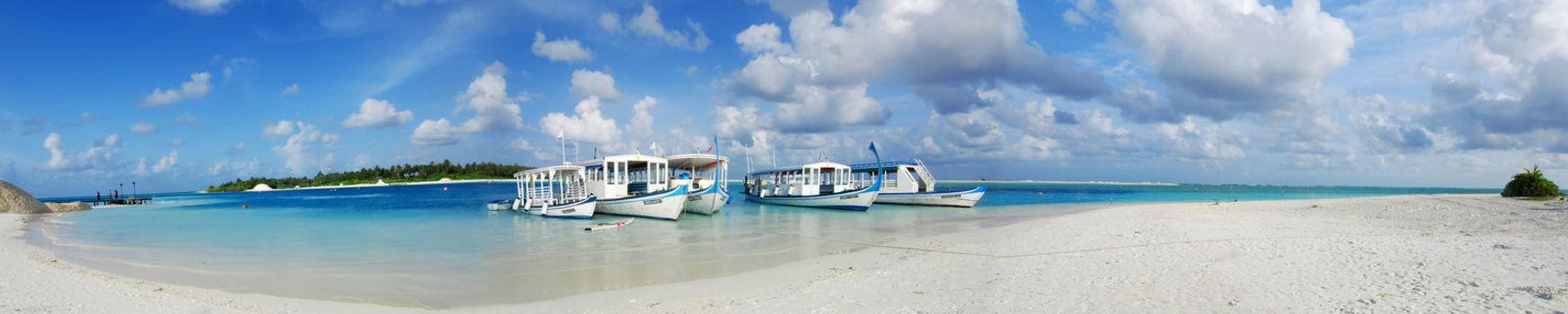 Beautiful white Maldivian beach and five dhoni ships docked nearby