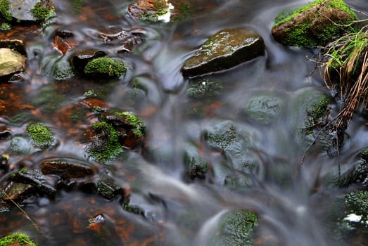 Hidden mountain brook with stones and moss with long exposure