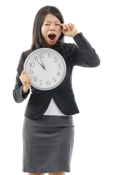 Tired Asian business woman holding a clock and rubbing eye, isolated on white background.
