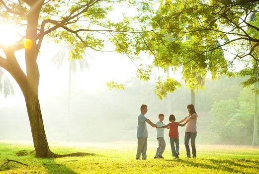 Happy Asian family holding hands in a circle and running over green lawn