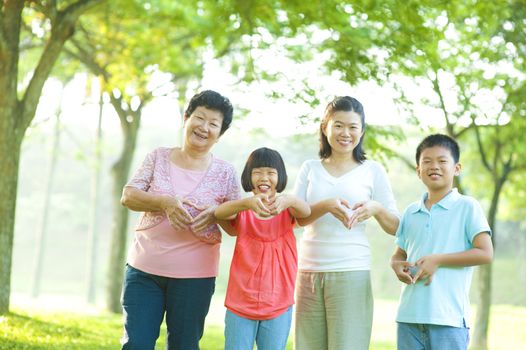 Happy playful Asian family forming love shape at outdoor green park
