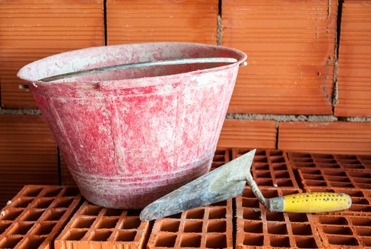 Trowel and bucket on a brick wall in a mansory workplace