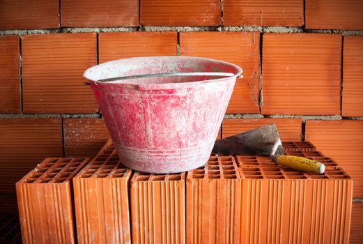 Trowel and bucket on a brick wall in a mansory workplace